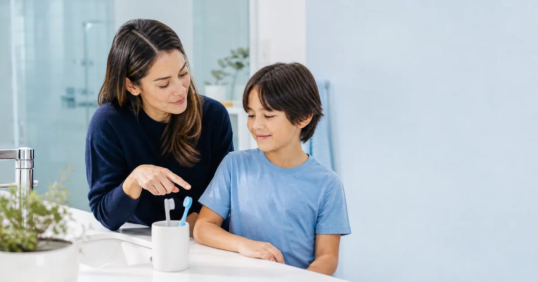 Parent and school-age child looking at two toothbrushes beside a bathroom sink.